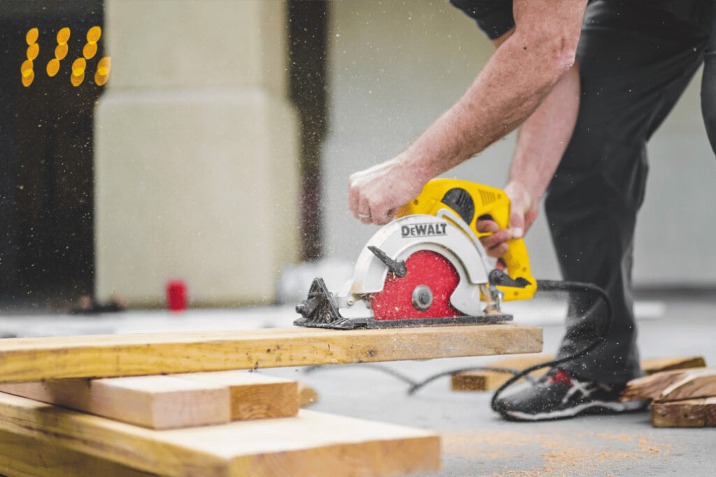 Construction worker using a circular saw to cut planks of wood.