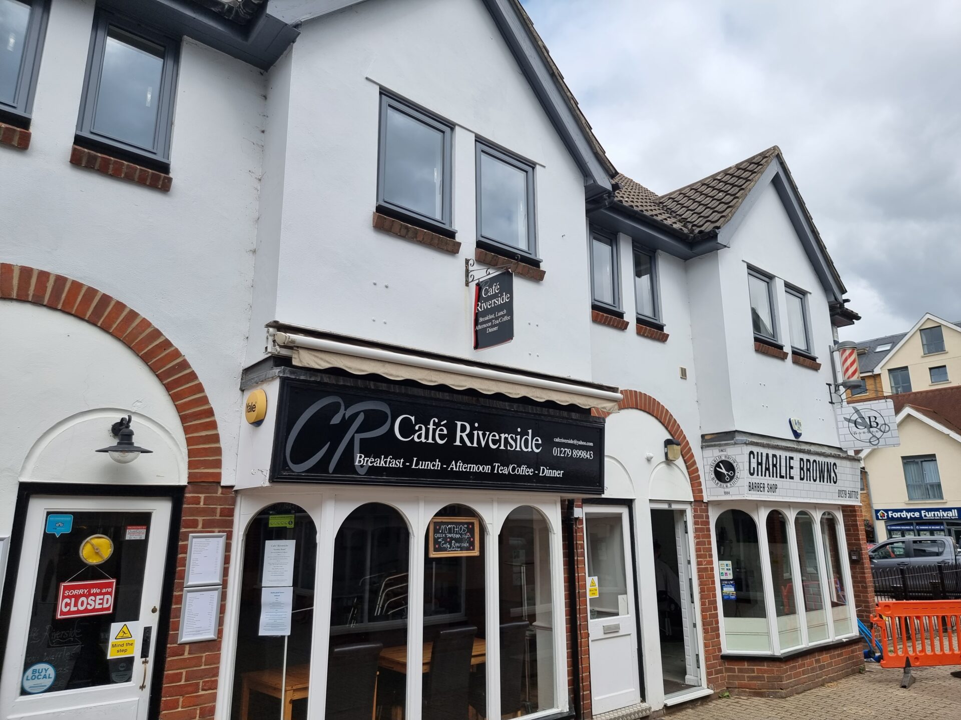 The front of Café Riverside, with the windows of the bottom floor showing an empty shop with tables and chairs.