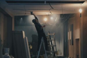 Photo by Henry & Co. on Unsplash of a man installing ceiling wiring in an office space. 